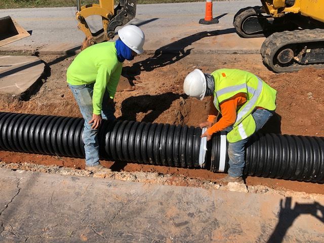 Two people work on a black pipe